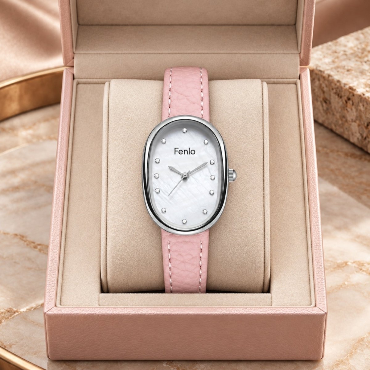 A pink leather strap wristwatch with an oval silver-tone case and a white dial, displayed inside an open blush pink presentation box. The brand name 'Fenlo' is visible on the watch face.