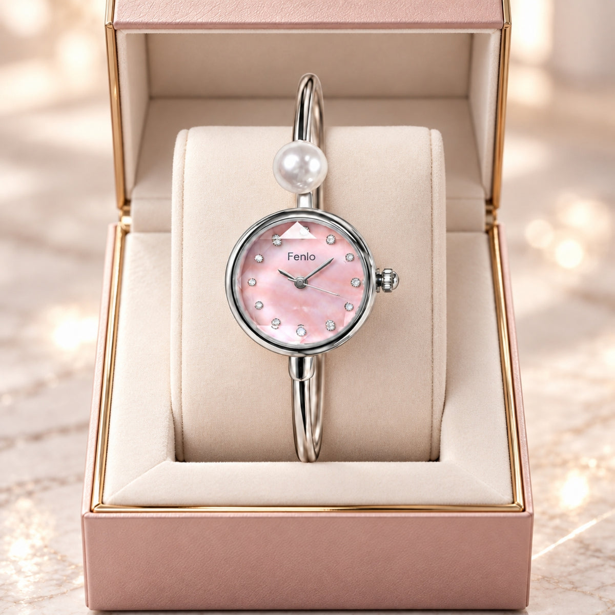 A Feniio women's bangle watch with a pink mother-of-pearl dial and a silver-toned bracelet with a pearl accent, presented inside an open pink jewelry box.