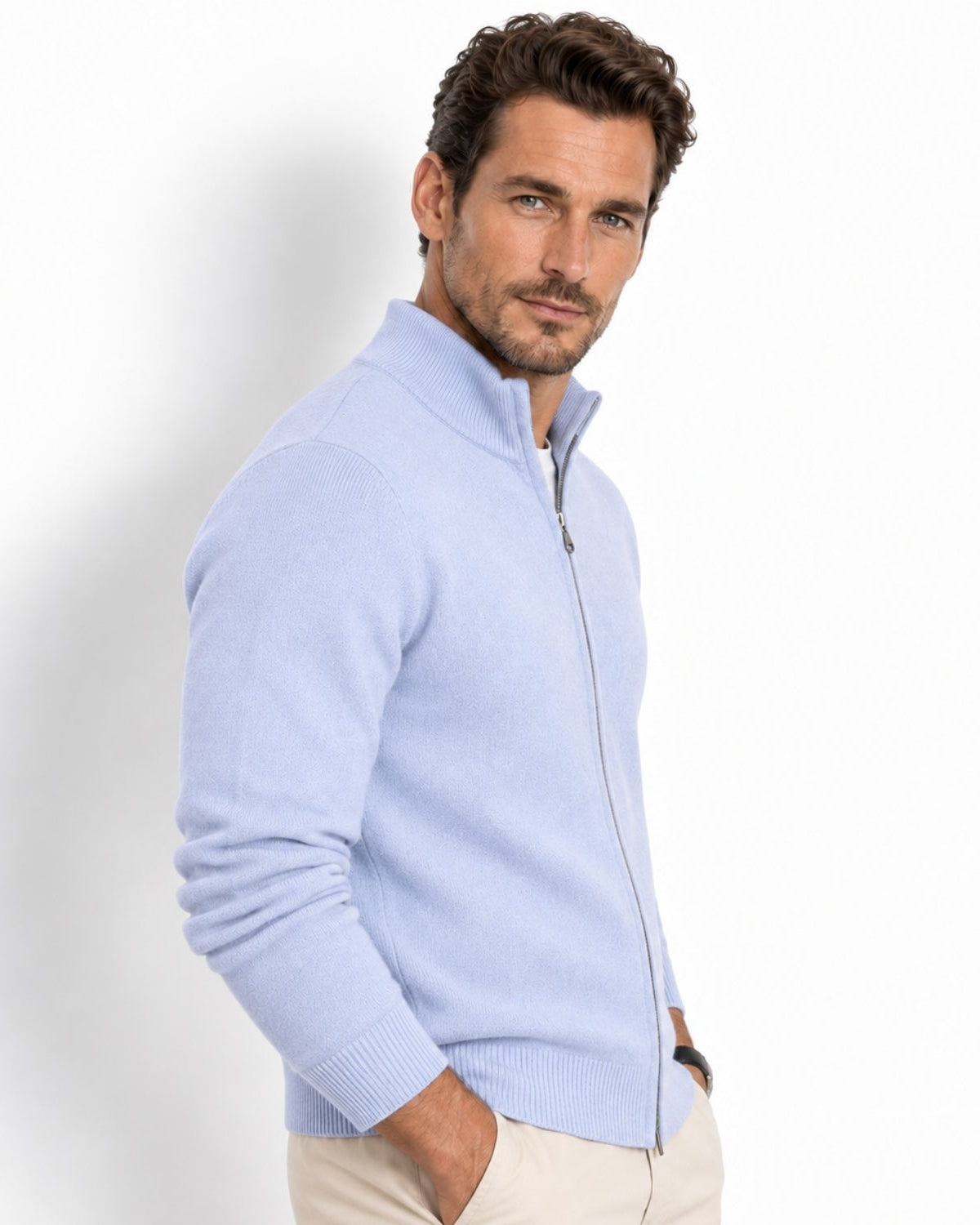 A man wearing a sky blue knit zip-up sweater with a mock neck collar, paired with beige trousers, photographed against a clean white studio background.