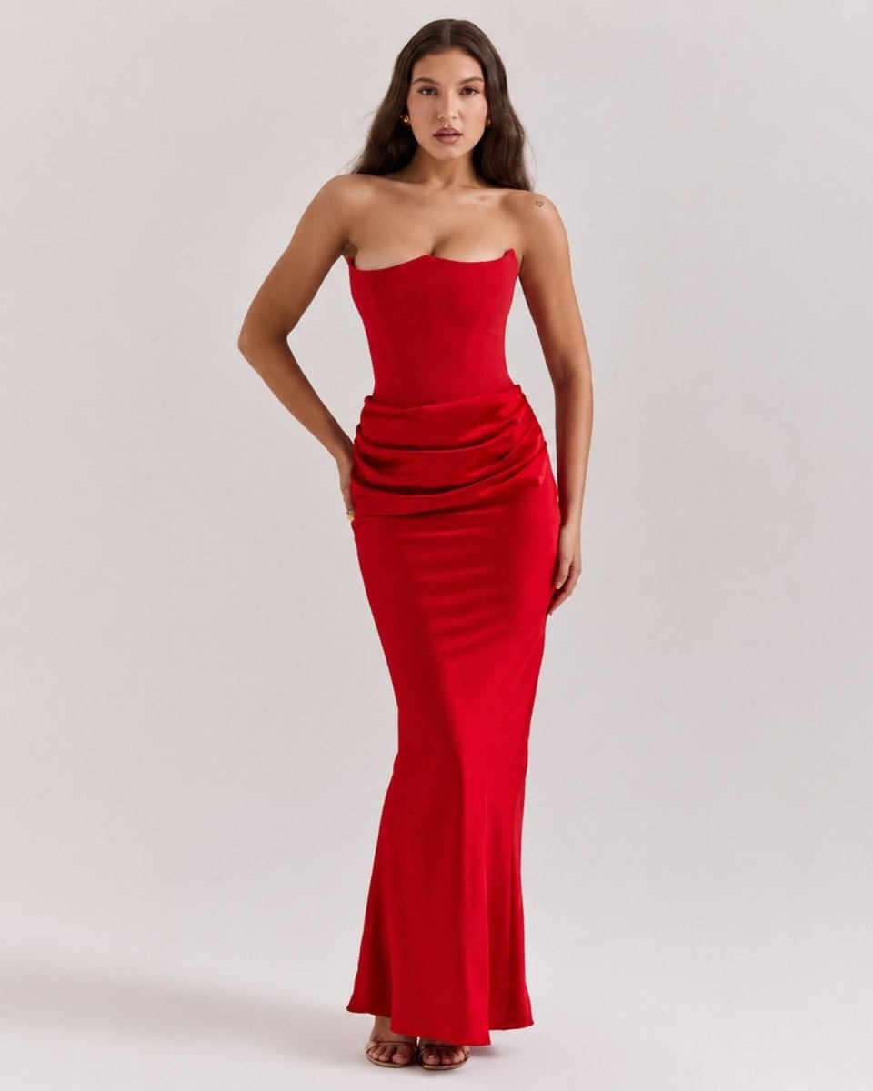 A woman modeling a strapless red maxi dress with a ruched waist and flared hem, photographed against a plain light gray studio background.