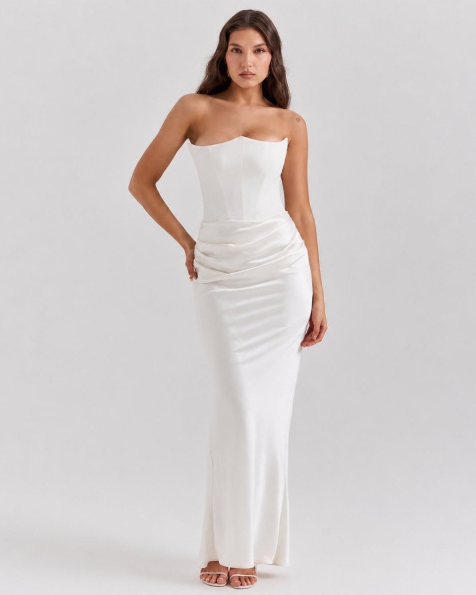 A woman modeling a strapless white maxi dress with a fitted bodice, ruched waist, and floor-length skirt against a light gray studio background.