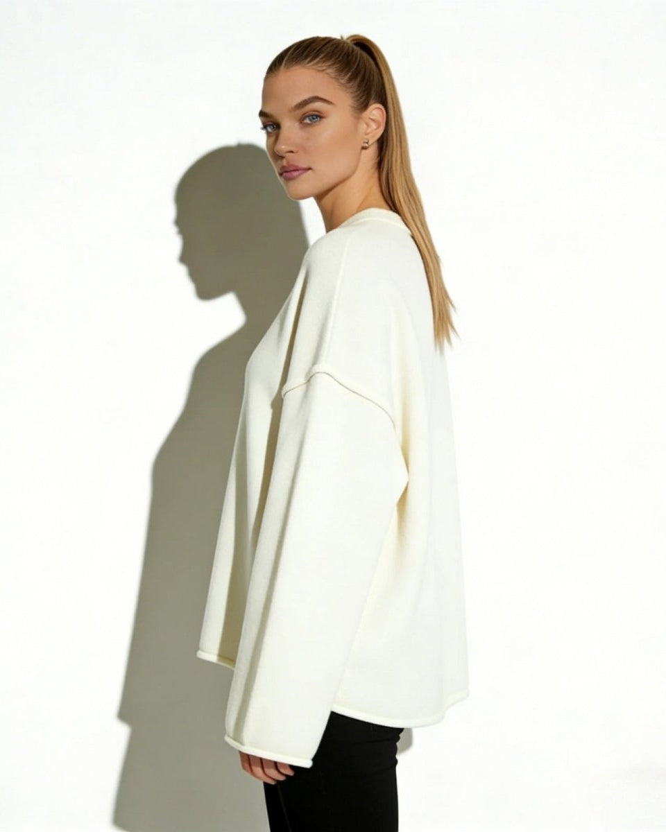 Side view of a woman in the oversized ivory wool-blend sweater, showcasing the wide sleeve silhouette and modern dropped shoulder detail.
