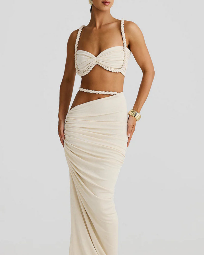 Model wearing The Thelma Set, a beige two-piece Grecian outfit featuring a rope detail bralette top and a ruched asymmetrical maxi skirt