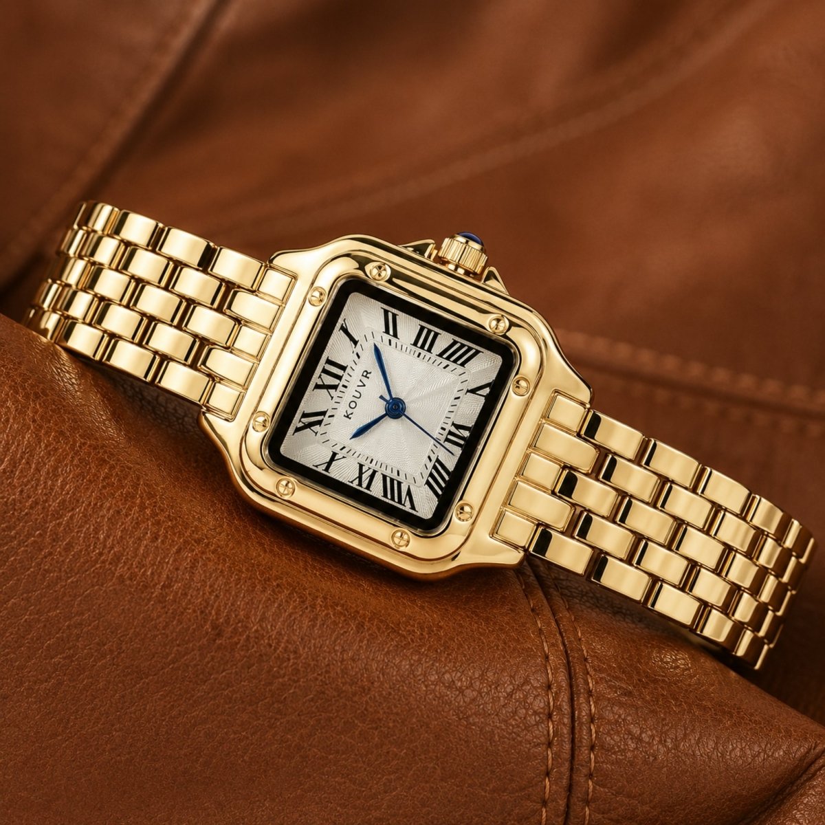 Elegant Kouvr gold-tone women's watch with blue cabochon crown resting flat on a sophisticated brown leather surface.