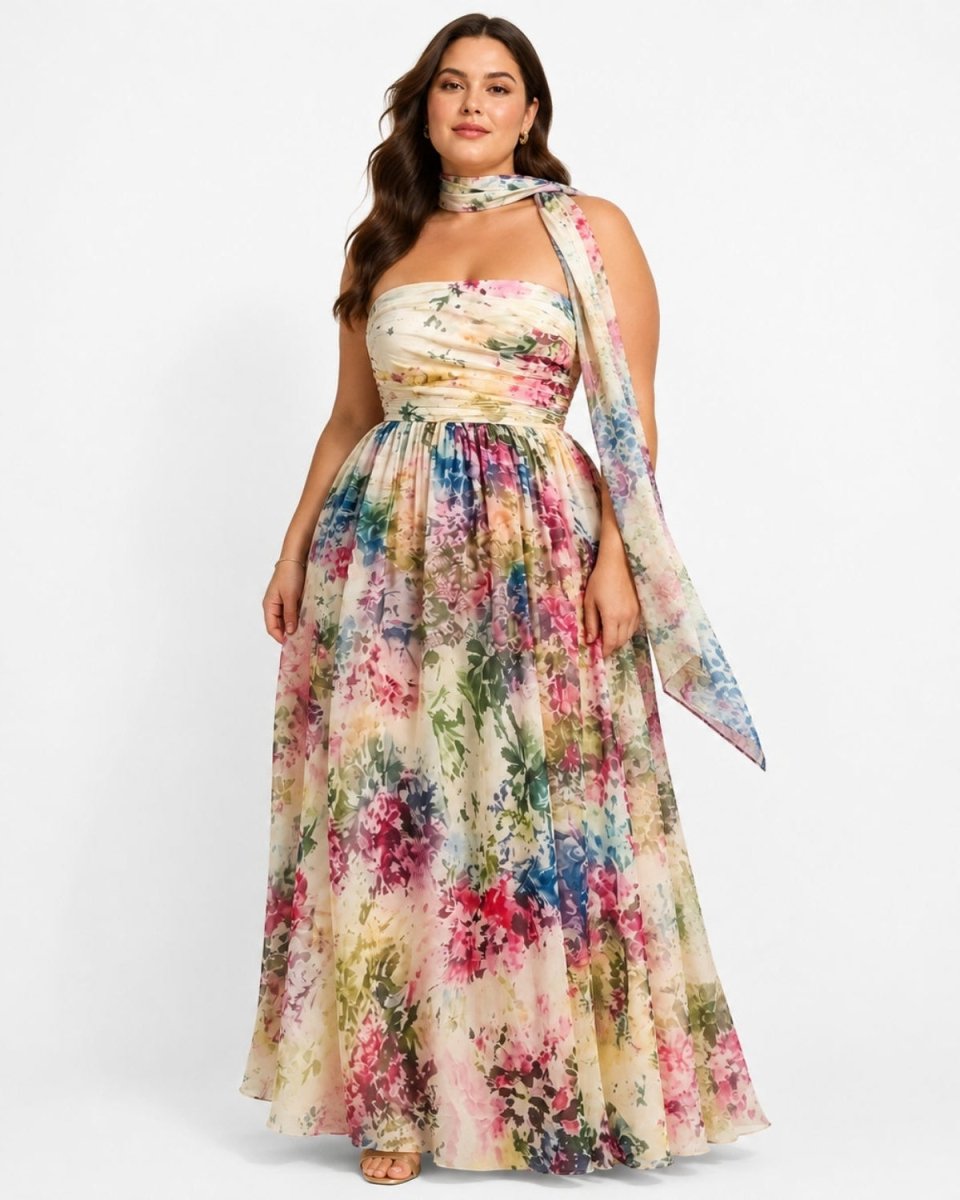 A woman modeling a strapless maxi dress with a matching draped scarf. The dress features a cream-colored base with a vibrant, multicolored floral print in pink, blue, green, and yellow.