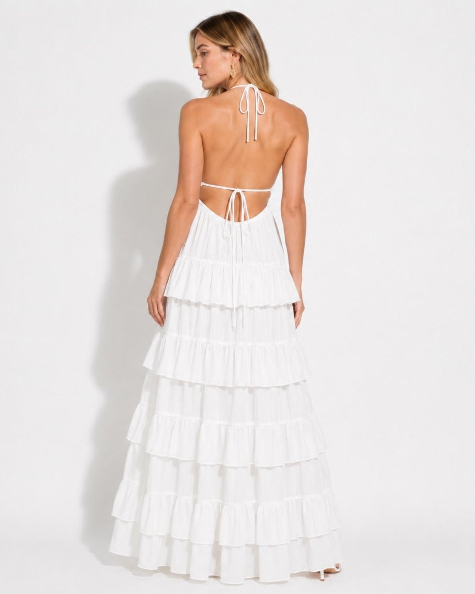 Back view of a woman in a white backless tiered summer maxi dress, showing the delicate back ties and luxurious fabric flow.