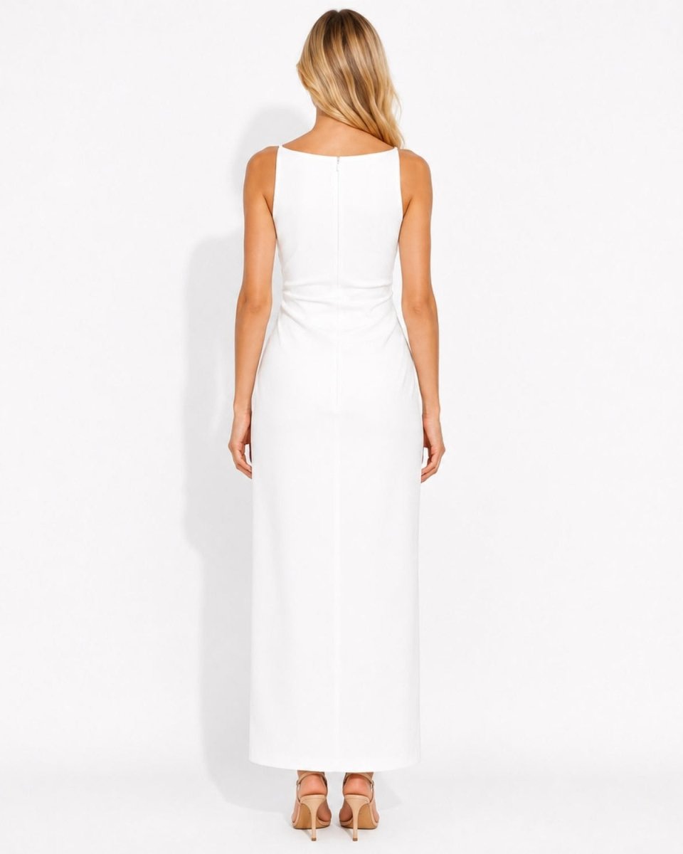 A woman viewed from the back wearing a sleeveless white maxi dress and nude high heels against a plain white studio background.