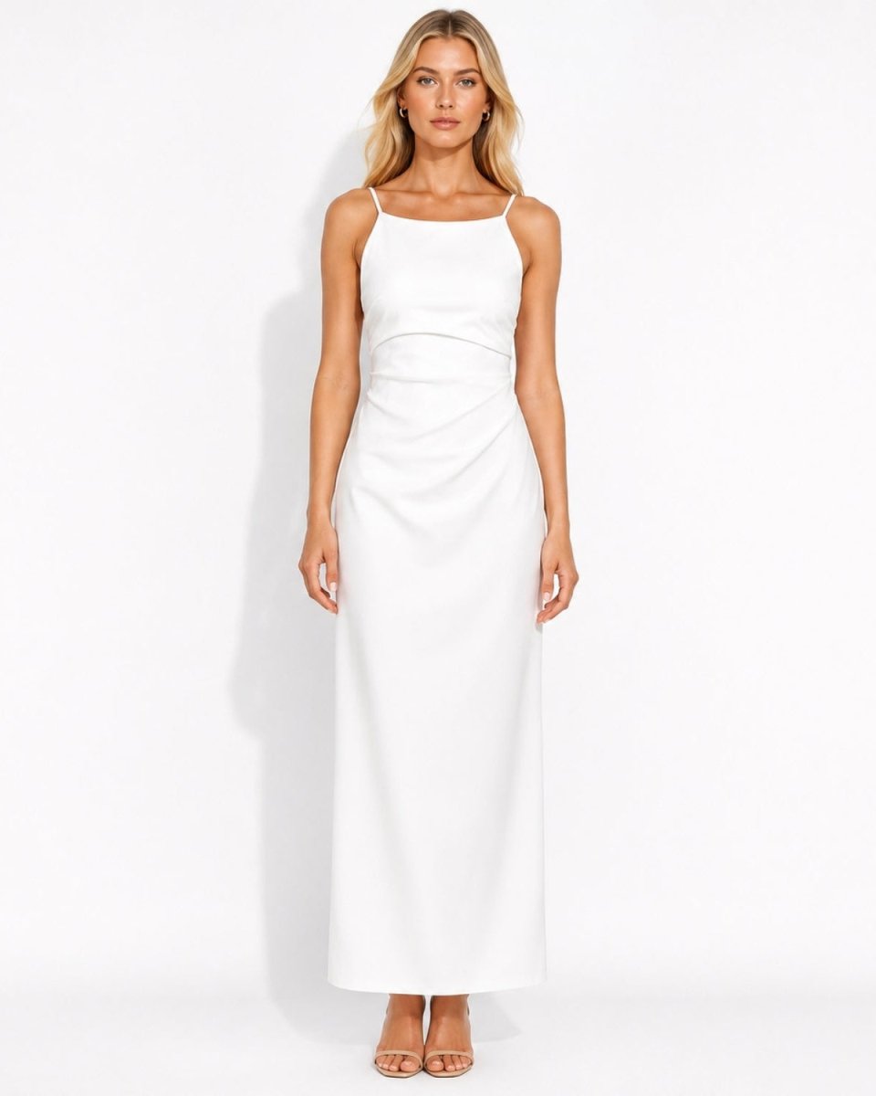 A woman modeling a white sleeveless maxi dress with thin spaghetti straps and a draped waist detail, standing against a clean white studio background.
