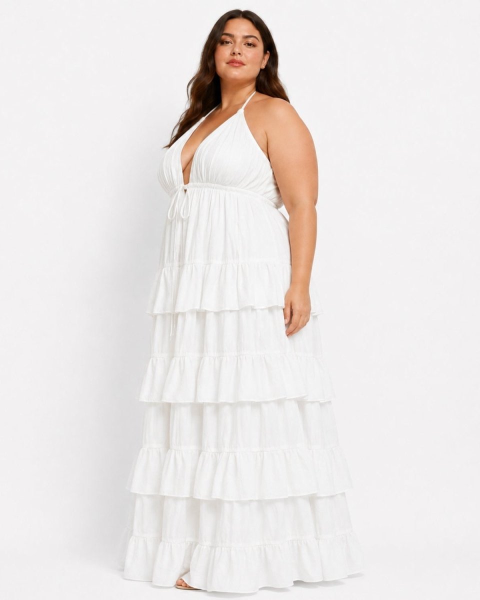 A woman modeling a white halter-neck maxi dress with a tiered ruffle skirt against a plain white studio background.
