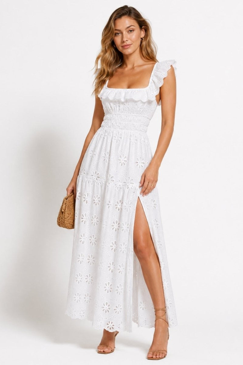 Woman wearing Kouvr white eyelet lace maxi dress with high side slit and ruffle square neckline, holding a woven clutch handbag.