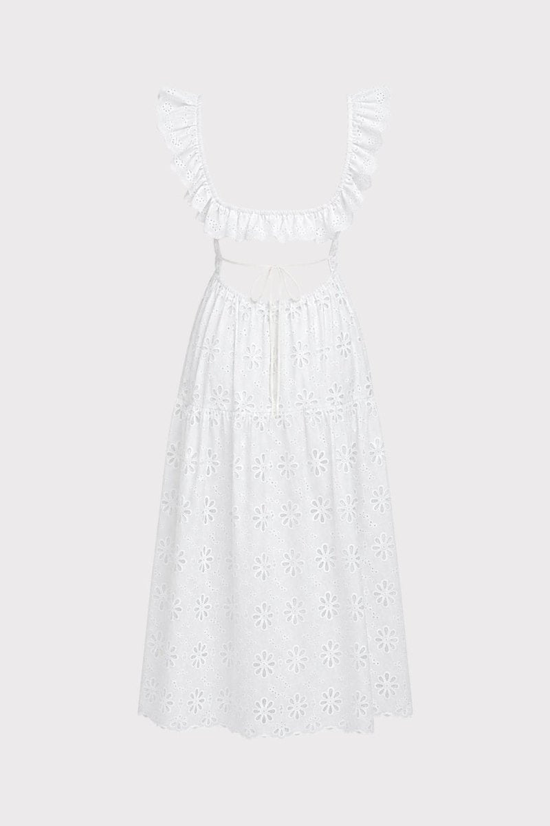 Studio shot detailing the back view of a white open back tie dress with intricate eyelet floral embroidery on a light grey background.