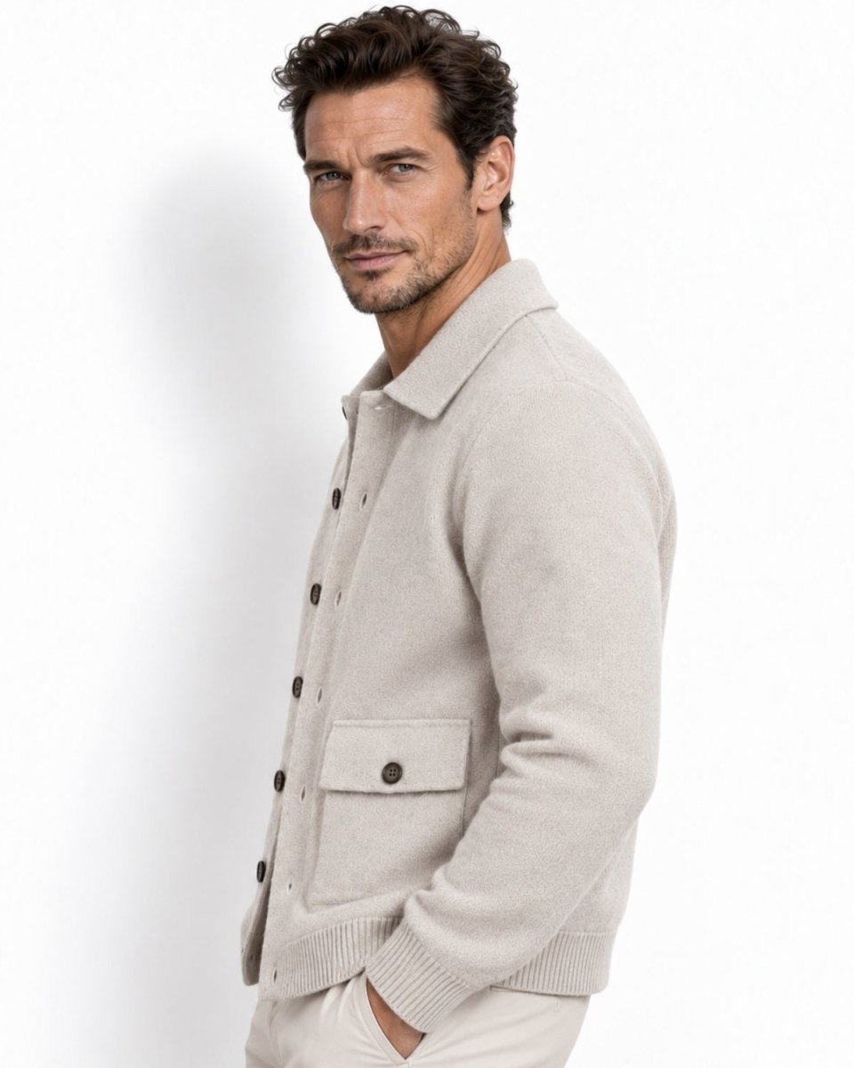 A man wearing a white knit button-up cardigan sweater with dark buttons and a collar, paired with light trousers, photographed against a clean white background.