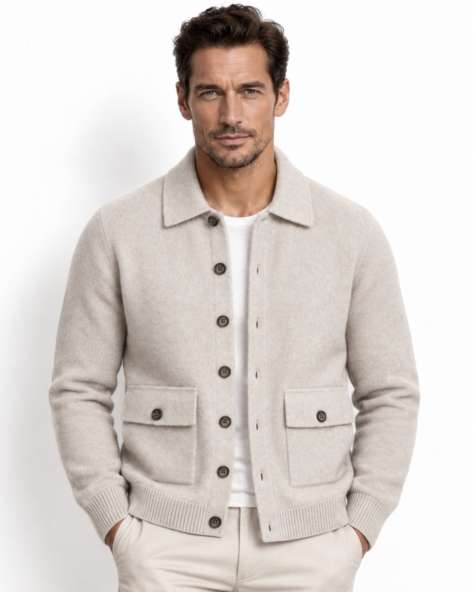 A man wearing a white knit button-up cardigan over a white t-shirt and cream trousers, standing against a plain white studio background.