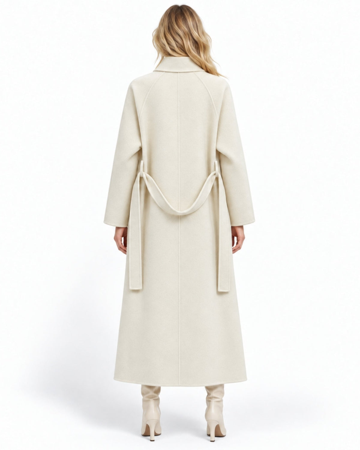 A woman viewed from the back wearing a long cream-colored wrap coat with a matching waist tie, paired with matching cream ankle boots, against a plain white studio background.