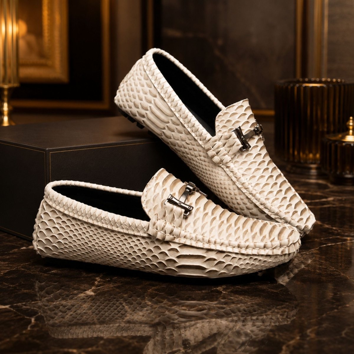 A pair of off-white snakeskin-patterned loafers with silver-tone metal hardware, displayed on a dark marble surface with a black box in the background.