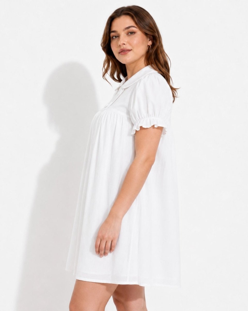 A woman modeling a white short-sleeve babydoll dress with a ruffled collar and sleeve cuffs, standing against a plain white studio background.