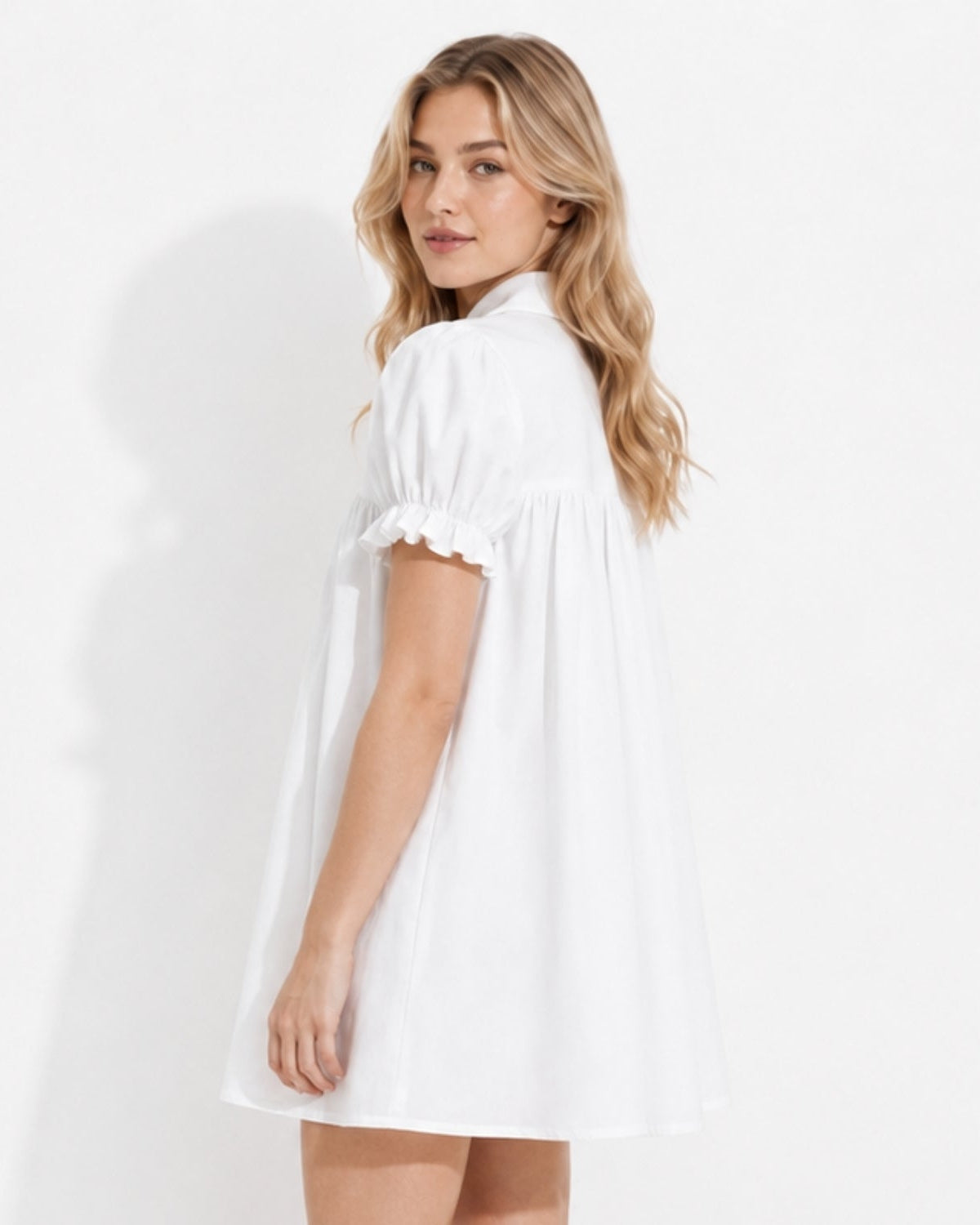 Side angle showing the drape of the white romantic coquette smock dress, emphasizing the lightweight fabric and ruffled arm cuffs.