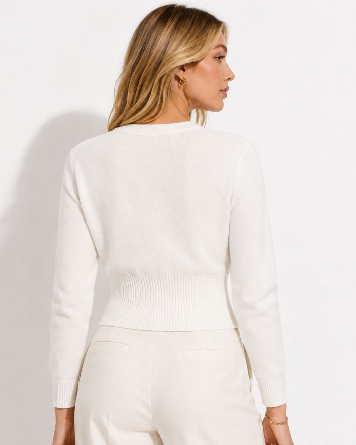 A woman shown from the back wearing a cream knit sweater and matching cream pants against a plain white studio background.