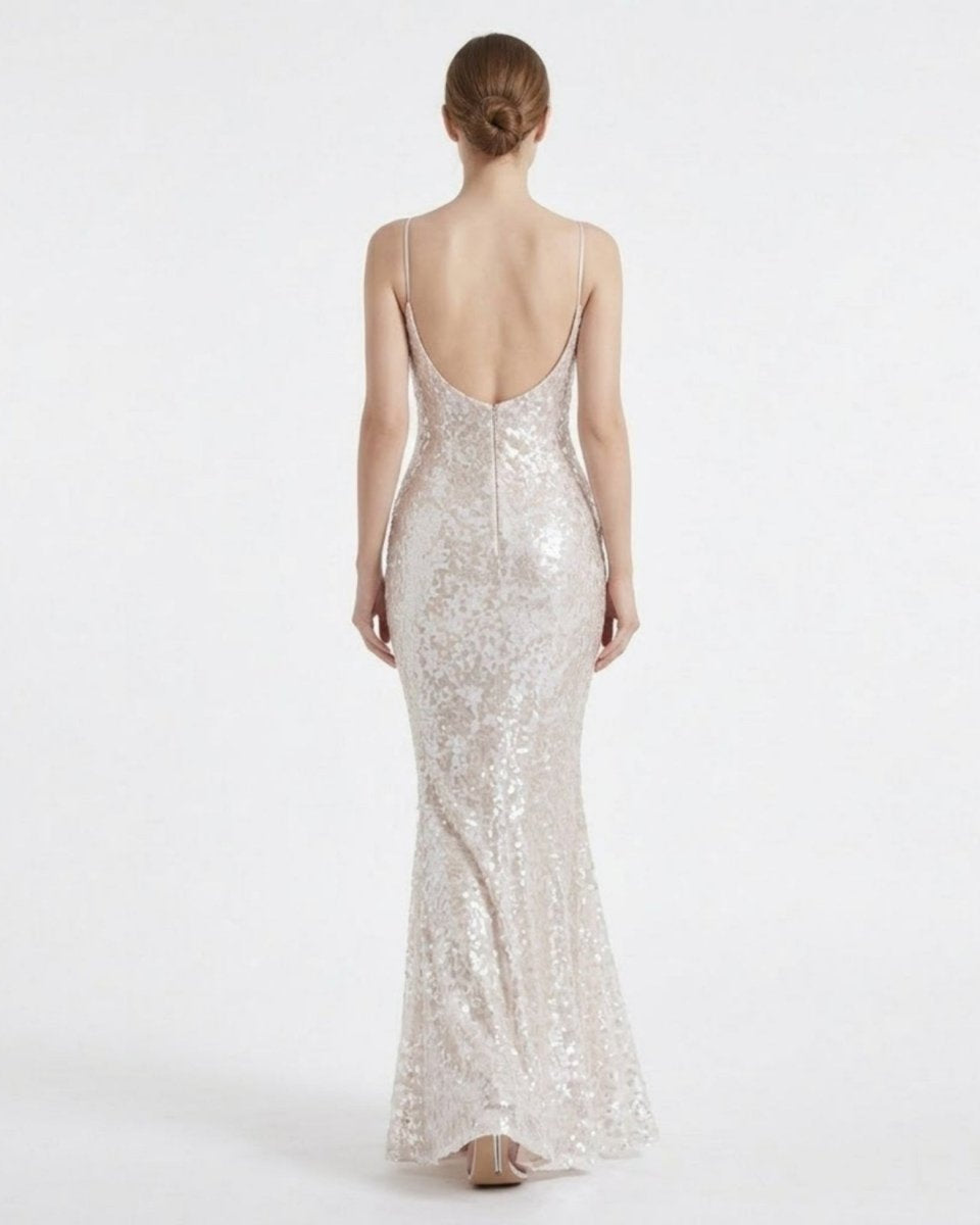 Back view of a female model wearing a backless white sequin formal dress, highlighting the deep V open back design and mermaid skirt flare.