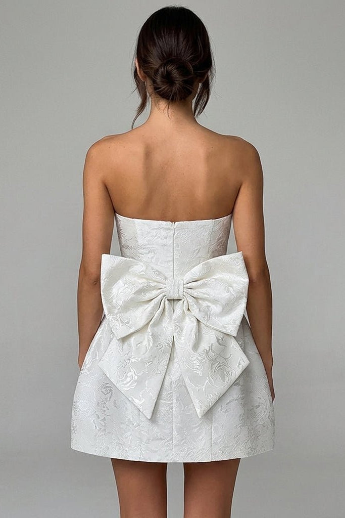Back view of white strapless mini dress featuring a dramatic oversized bow detail and invisible zipper
