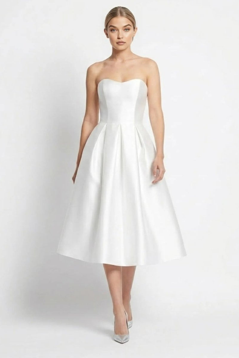 Woman walking wearing a white strapless satin midi dress with pleated A-line skirt by Fenlo Form.