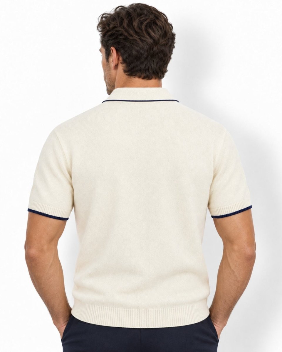 A man viewed from the back wearing a white-colored short-sleeve knit polo shirt with navy blue trim on the collar and sleeve cuffs, paired with dark navy trousers, against a clean white background.