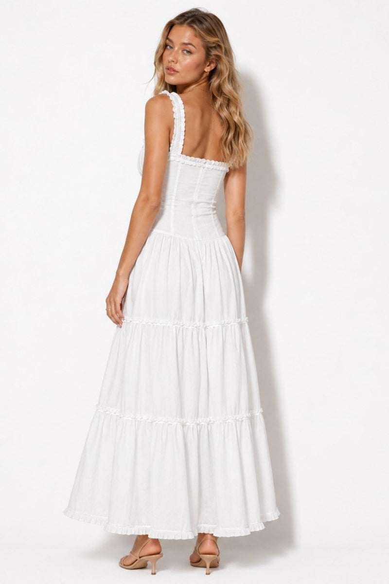 Woman looking over shoulder wearing a white tiered ruffle maxi dress showing the tailored corset back and wide ruffle straps.