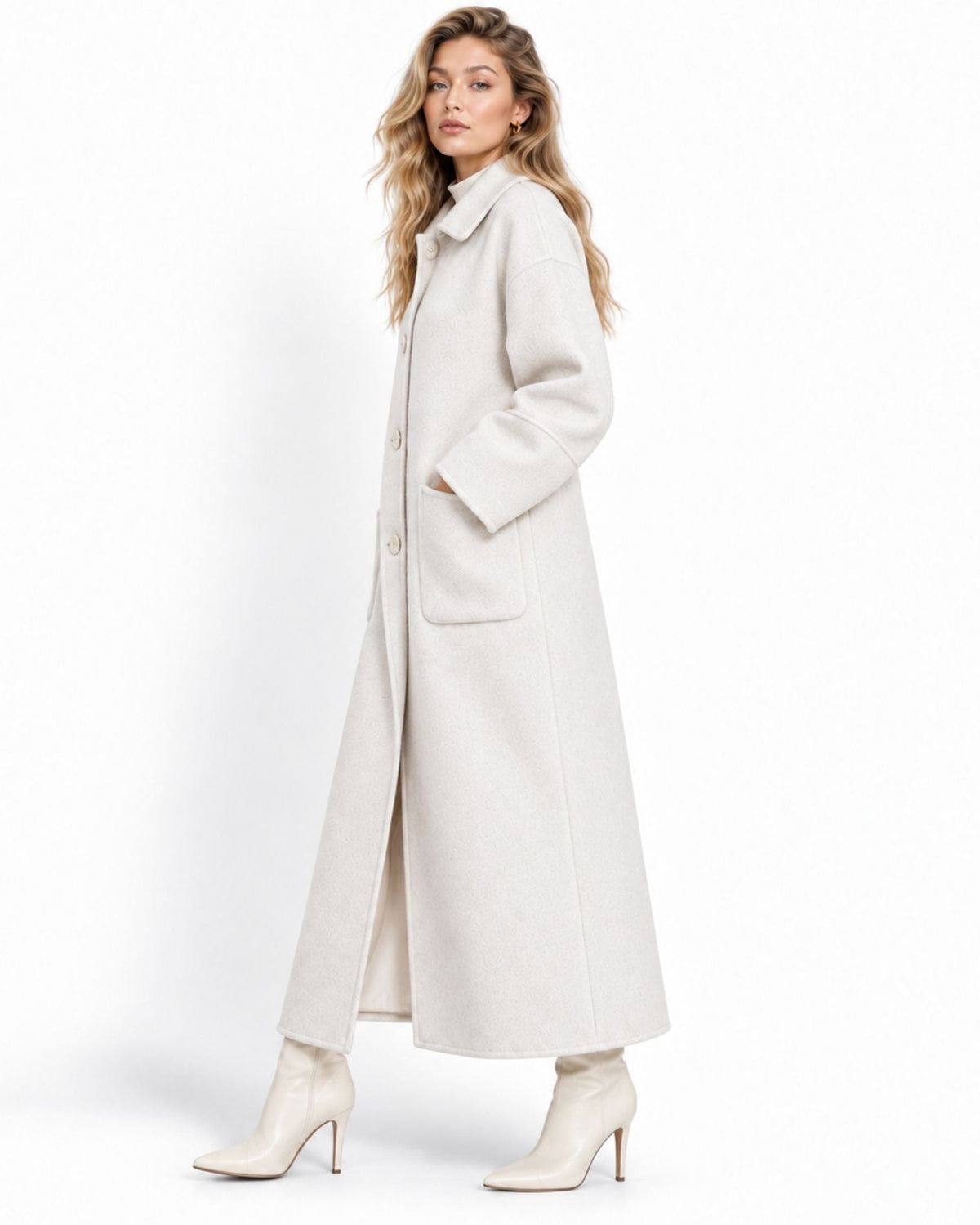 A woman modeling a long, light beige wool-blend coat with a high collar, front buttons, and large patch pockets, paired with matching beige ankle boots, against a plain white studio background.