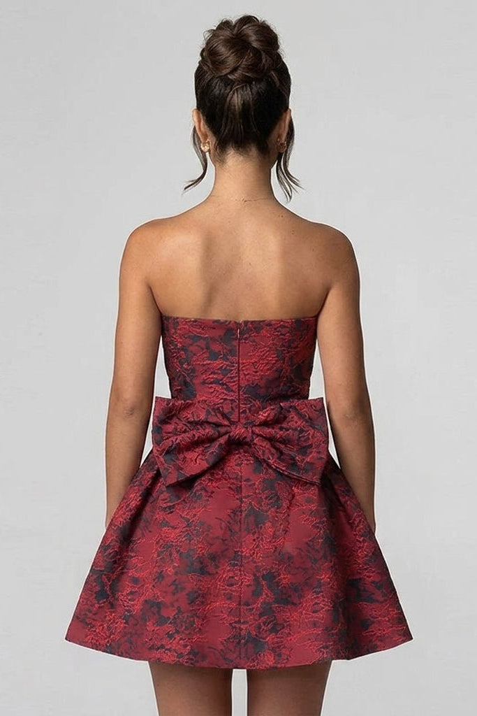 Back view of a wine red floral jacquard mini dress showcasing a dramatic oversized statement back bow and concealed zipper closure.