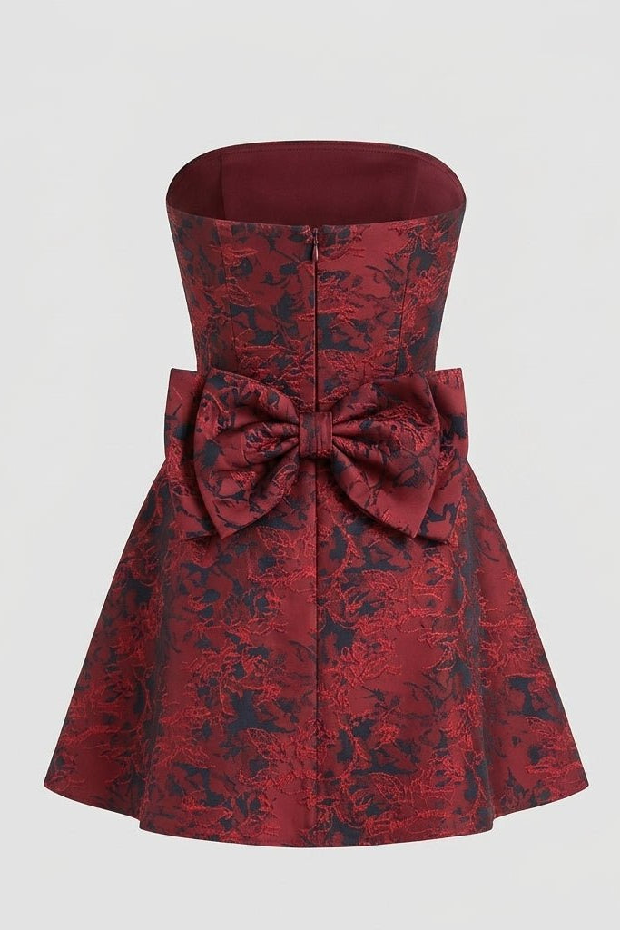 Back view of the red floral jacquard strapless mini dress on a ghost mannequin detailing the large attached bow and zipper.