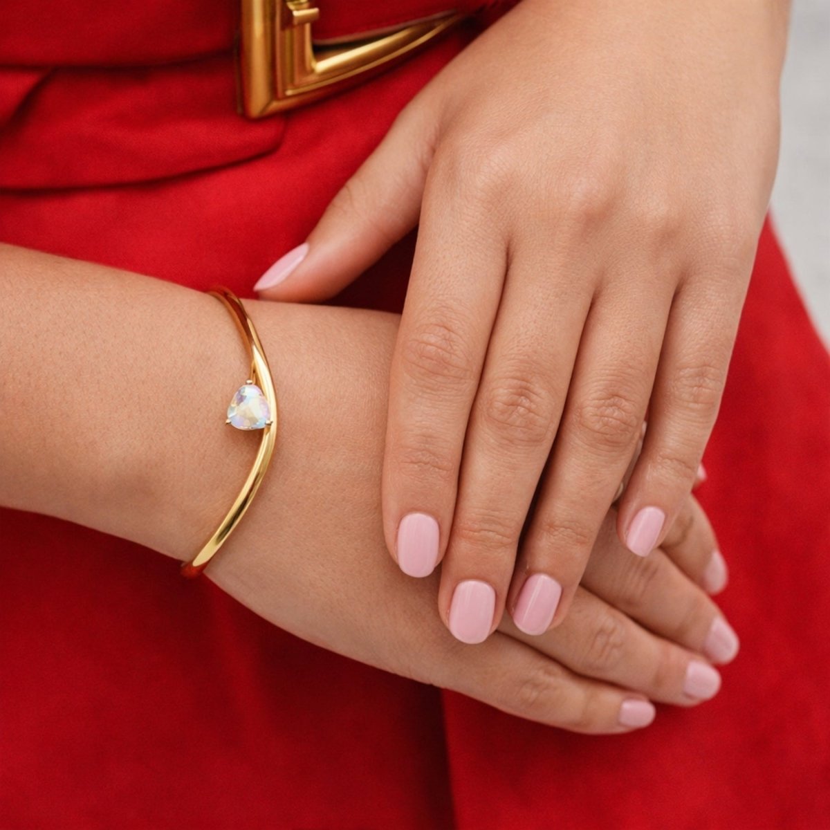A woman with light pink nail polish wearing the Kouvr Yelena gold wave bangle, shown with a red dress. 