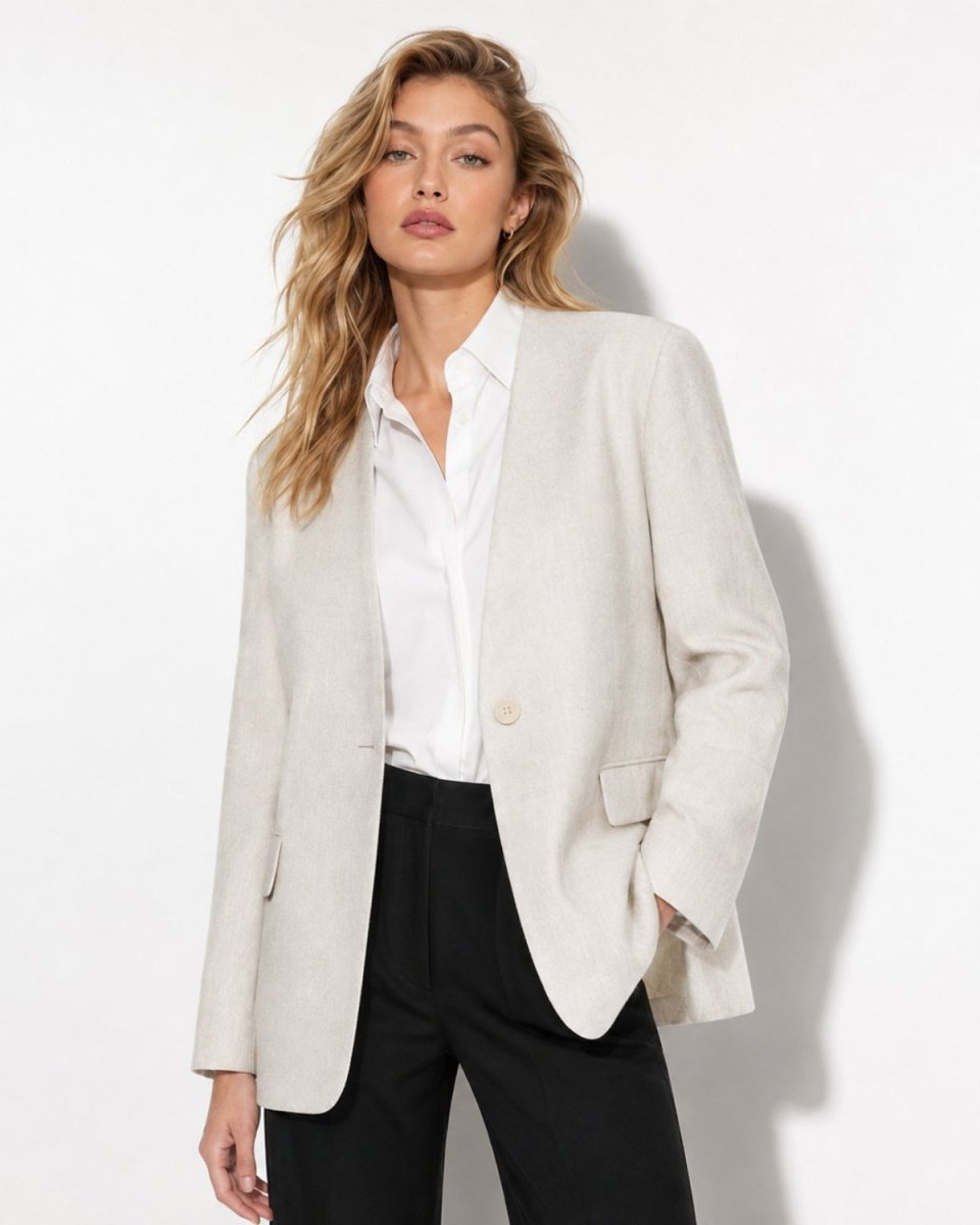A woman modeling an oversized light beige linen-blend blazer over a white button-down shirt and black trousers, photographed against a clean white studio background.