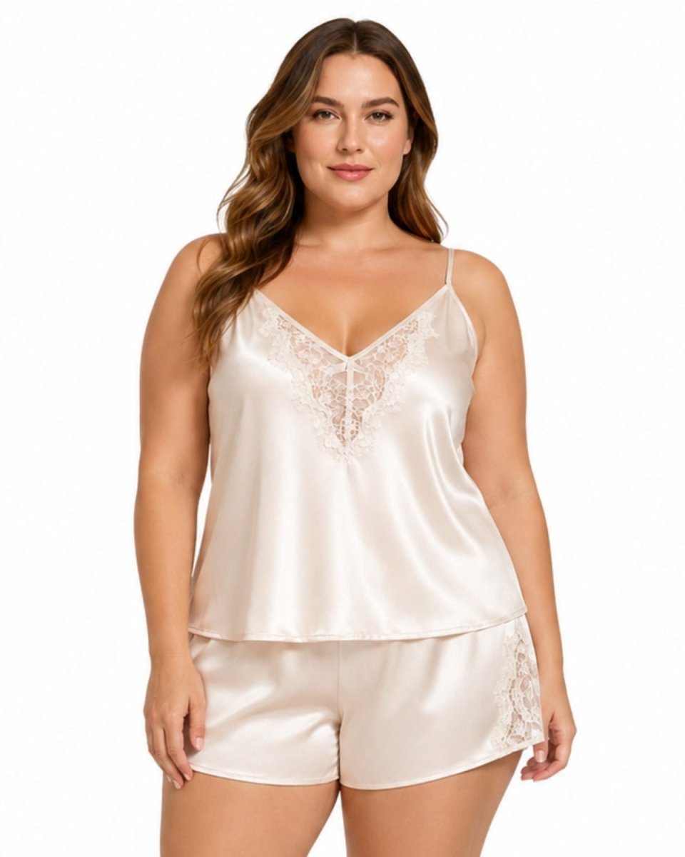 A woman modeling a satin sleepwear set consisting of a camisole top and matching shorts in a light champagne color with lace trim details, set against a plain white background.