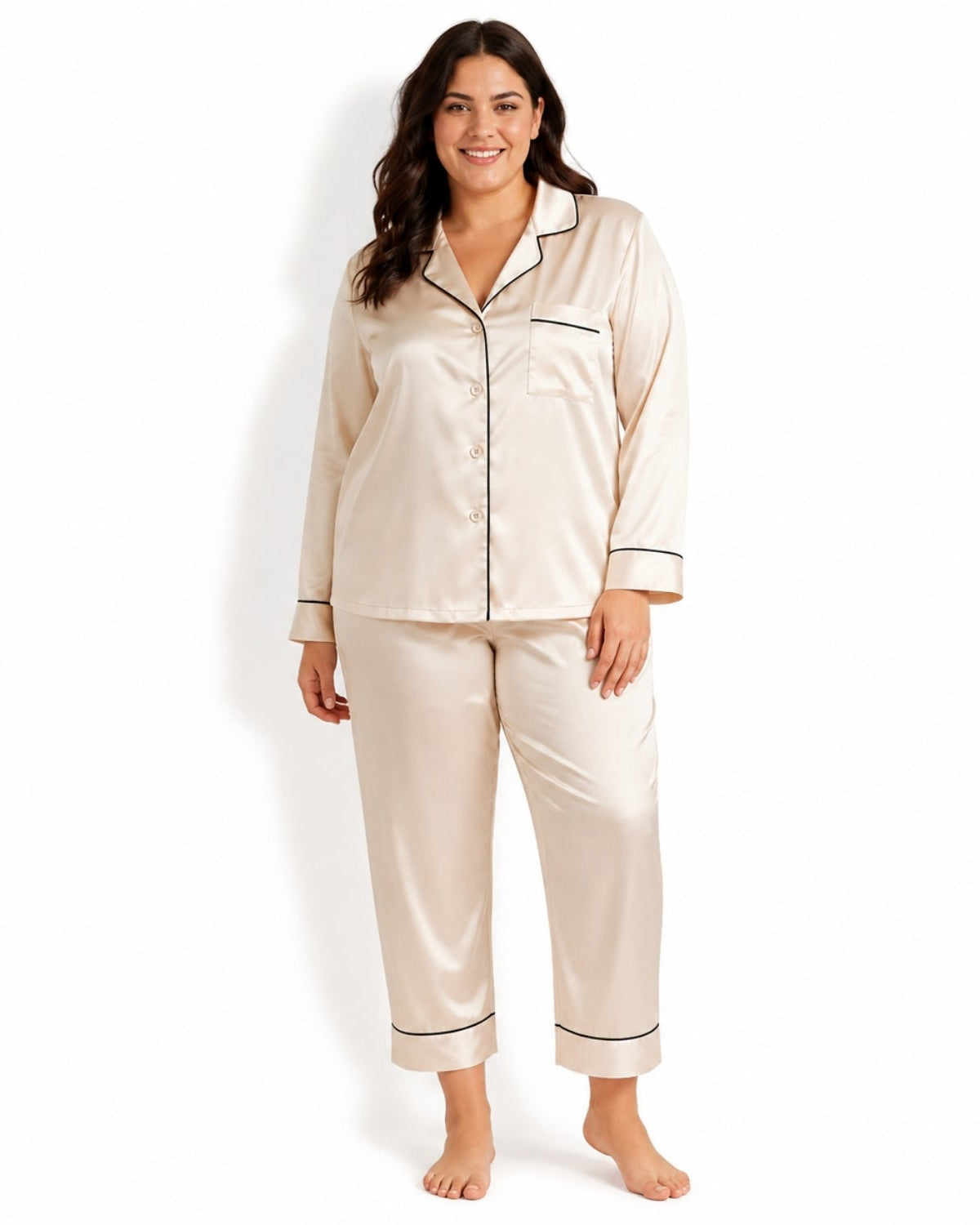 A woman modeling a two-piece satin pajama set in champagne beige with black piping, consisting of a long-sleeve button-front pajama top and matching pants, against a plain white background.