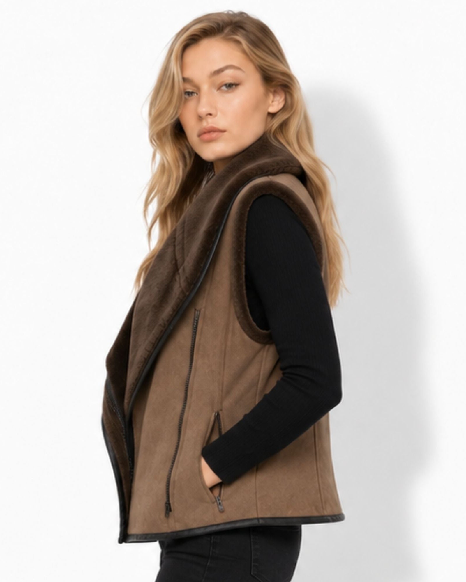 A woman wearing a brown suede-like sleeveless vest with a dark brown faux-fur collar, layered over a black long-sleeve top, photographed against a clean white studio background.