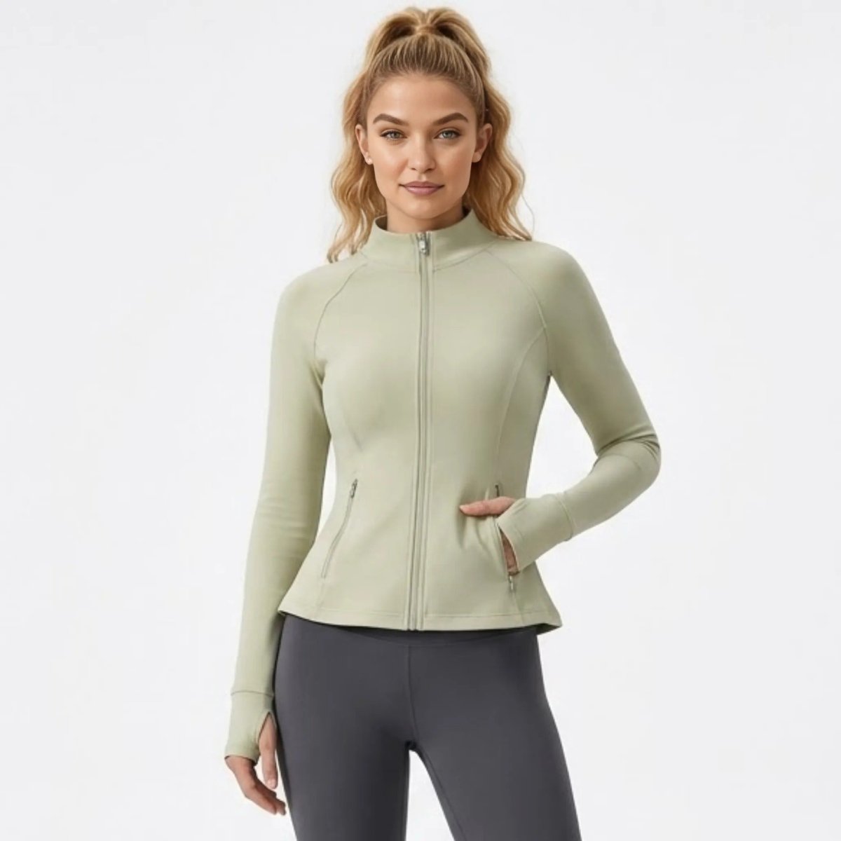  Front view of woman wearing a fitted green zip-up athletic jacket with high neck and thumbholes by Kouvr.