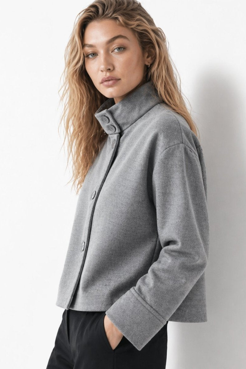  Side angle of a woman modeling a minimalist grey cropped jacket with wide sleeves and a high collar.