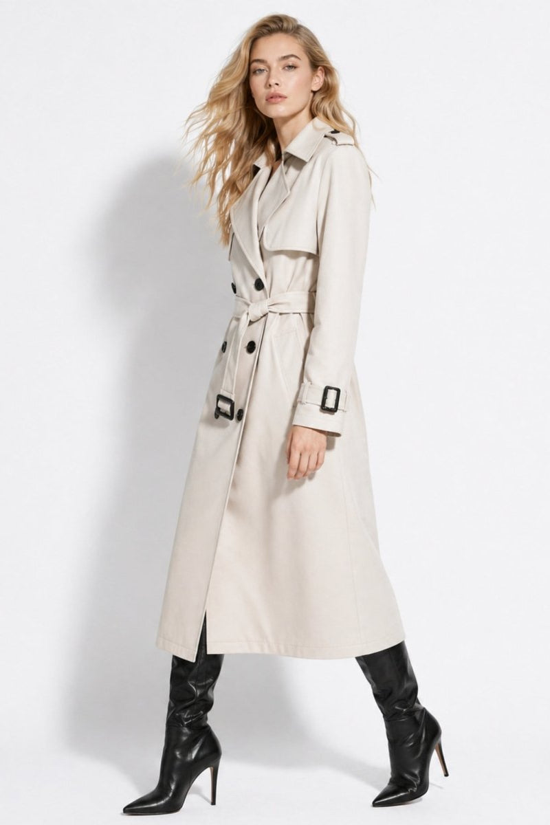 Fashion model walking confidently in a long belted stone ivory trench coat showing elegant movement, side profile, and sophisticated styling.
