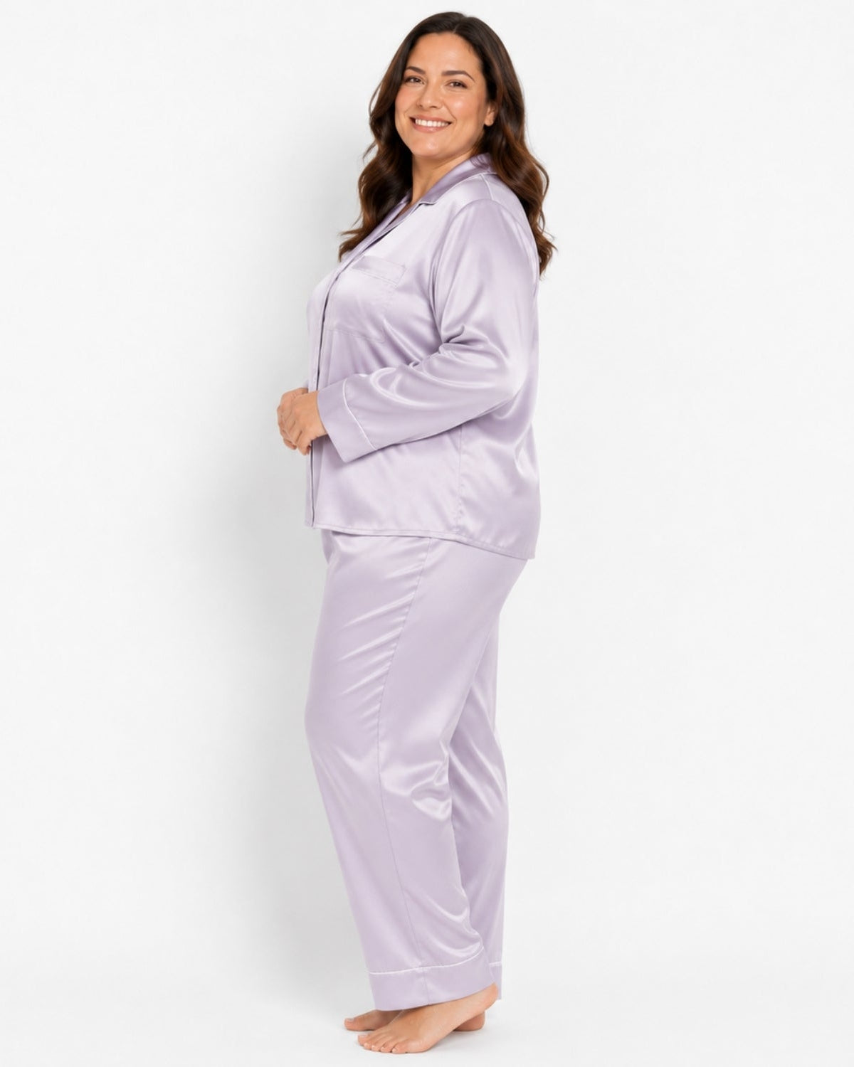 A woman modeling a two-piece satin pajama set in light lavender purple, standing against a plain white studio background.