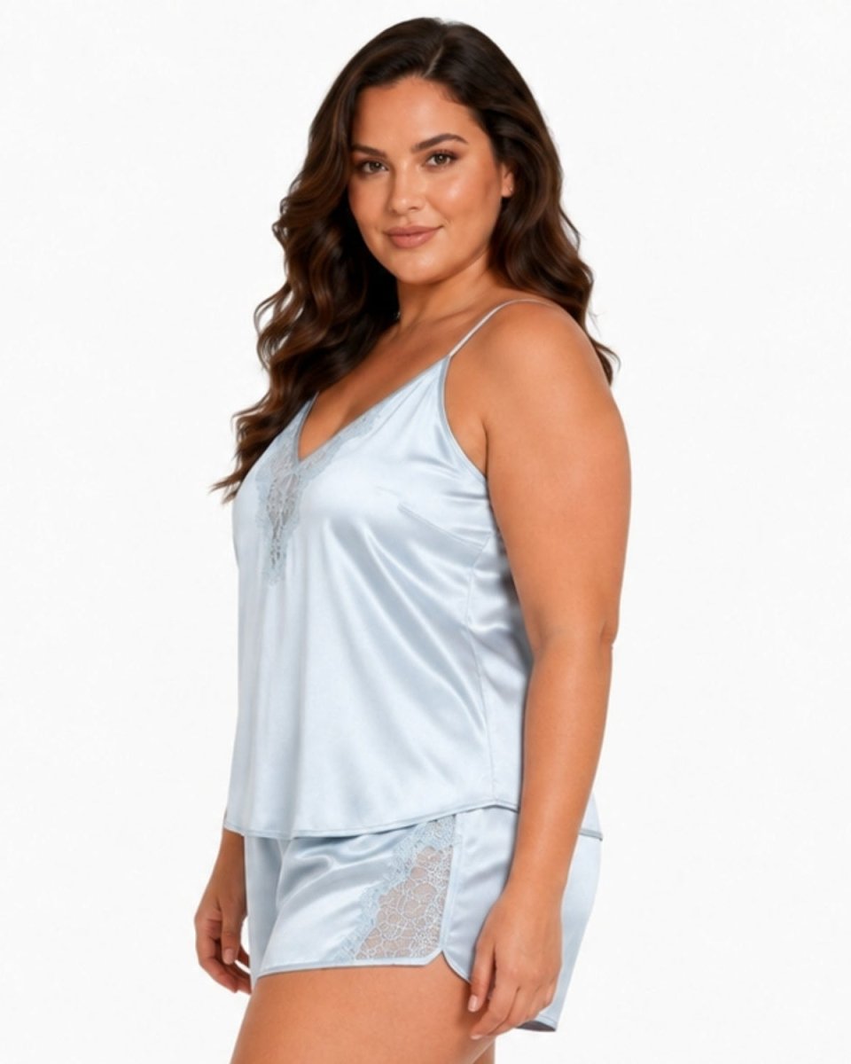 A woman modeling a light blue satin pajama set with a camisole top and matching shorts against a plain white background.