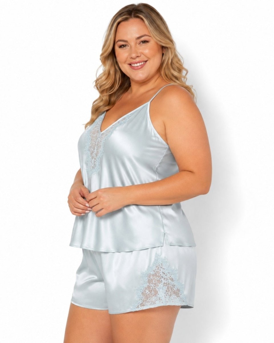 A woman modeling a light blue satin pajama set with lace trim, consisting of a camisole top and matching shorts, against a plain white background.
