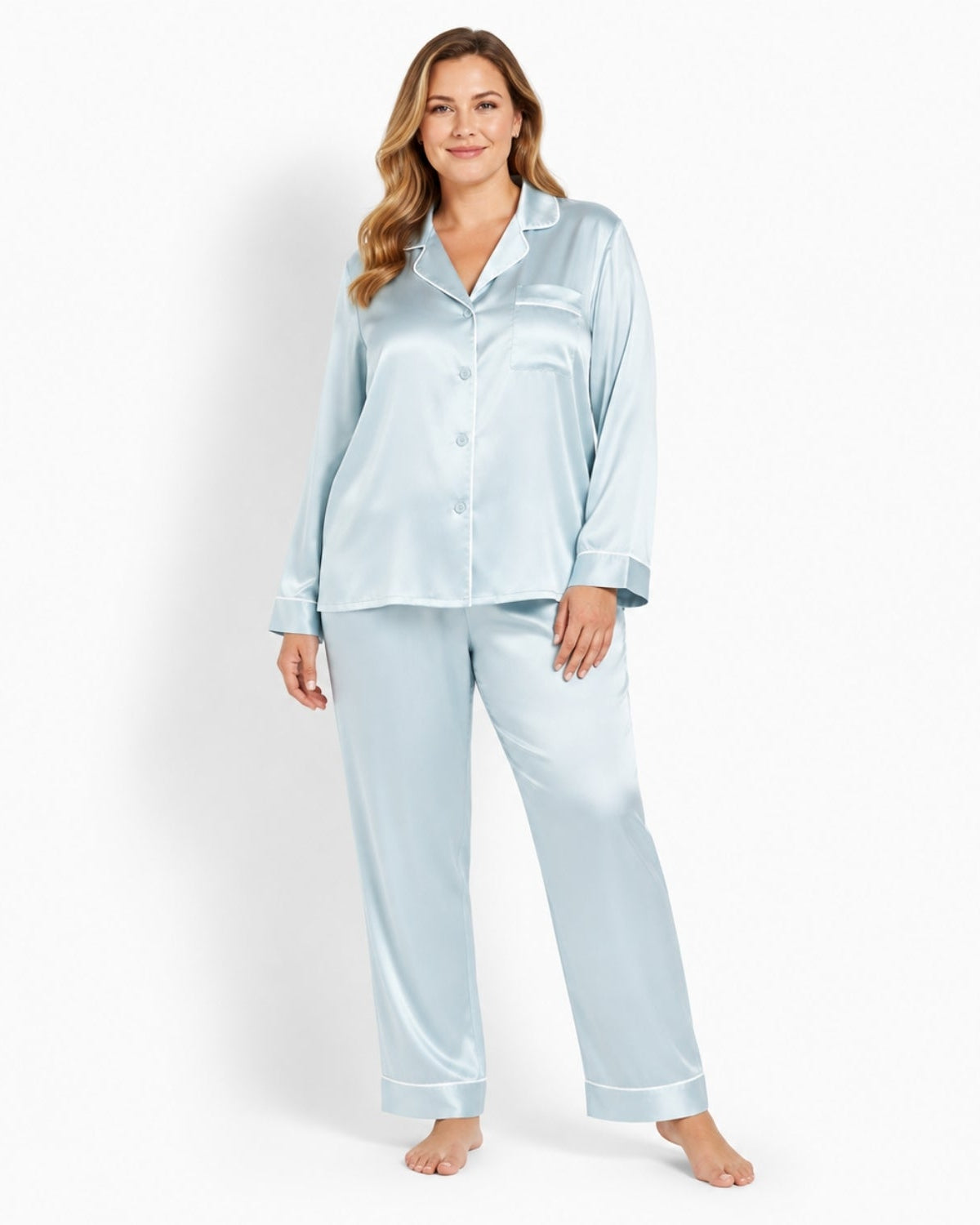 A woman modeling a light blue satin pajama set with a long-sleeve button-up shirt and matching pants against a plain white studio background.