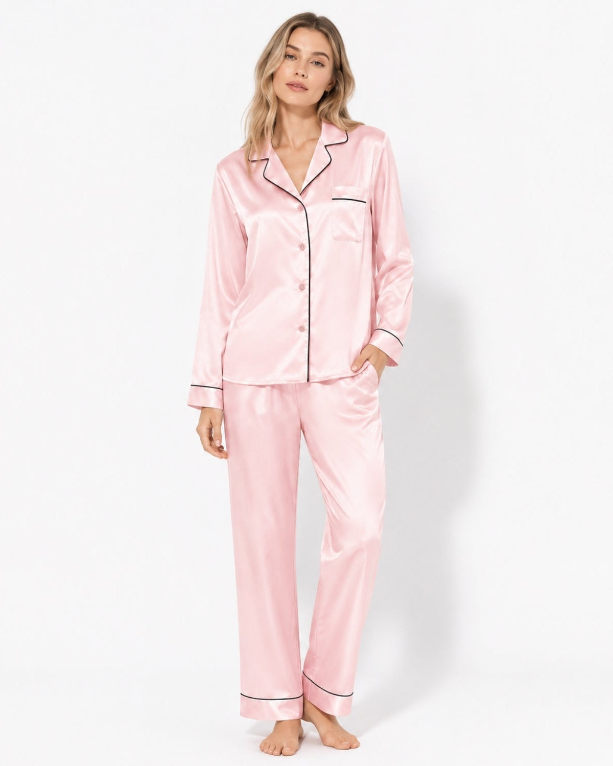 Woman modeling a luxury light pink silk satin pajama set with black contrast piping, long sleeve button down shirt and pants