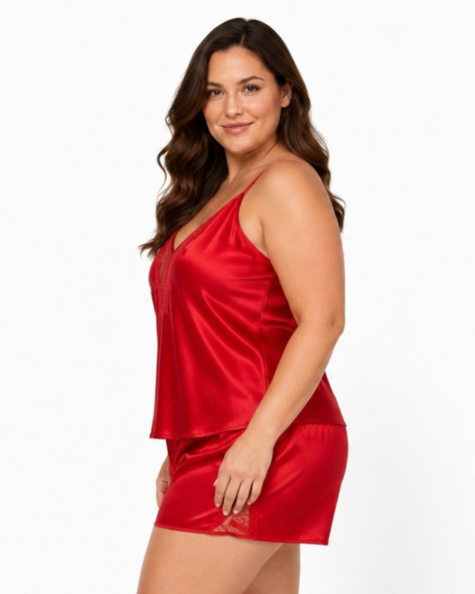 A woman modeling a two-piece red satin sleepwear set, consisting of a sleeveless camisole top and matching mini shorts, against a plain white studio background.
