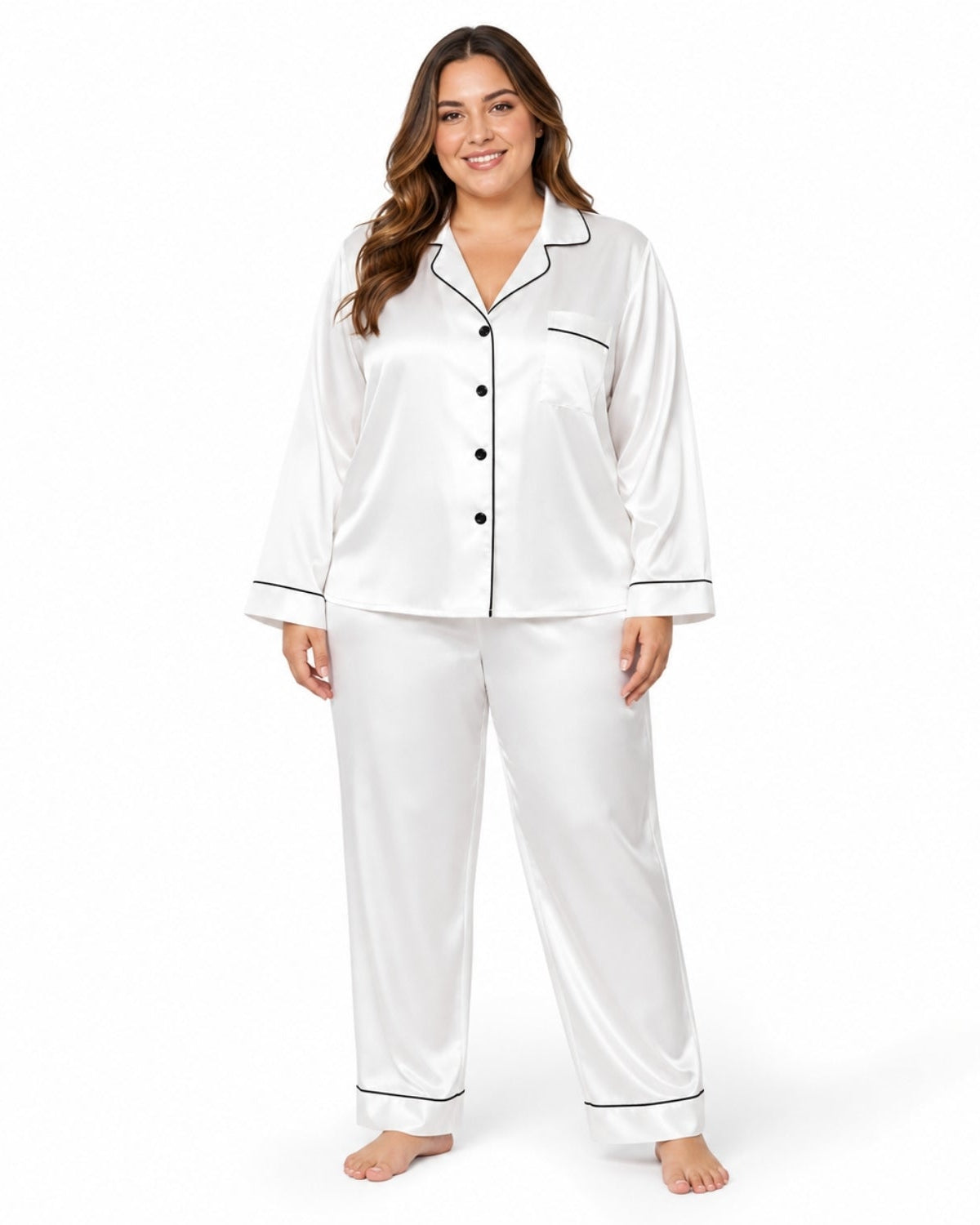 A woman modeling a two-piece white satin pajama set with black piping trim, consisting of a long-sleeve button-up top and matching pants, against a plain white background.