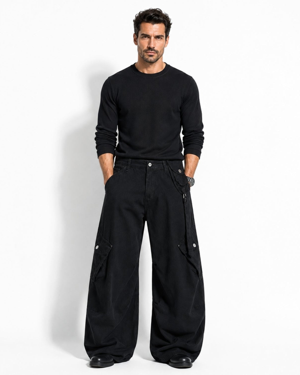 A man modeling a black long-sleeve crewneck shirt and black wide-leg cargo pants with side utility pockets, standing against a plain white studio background.