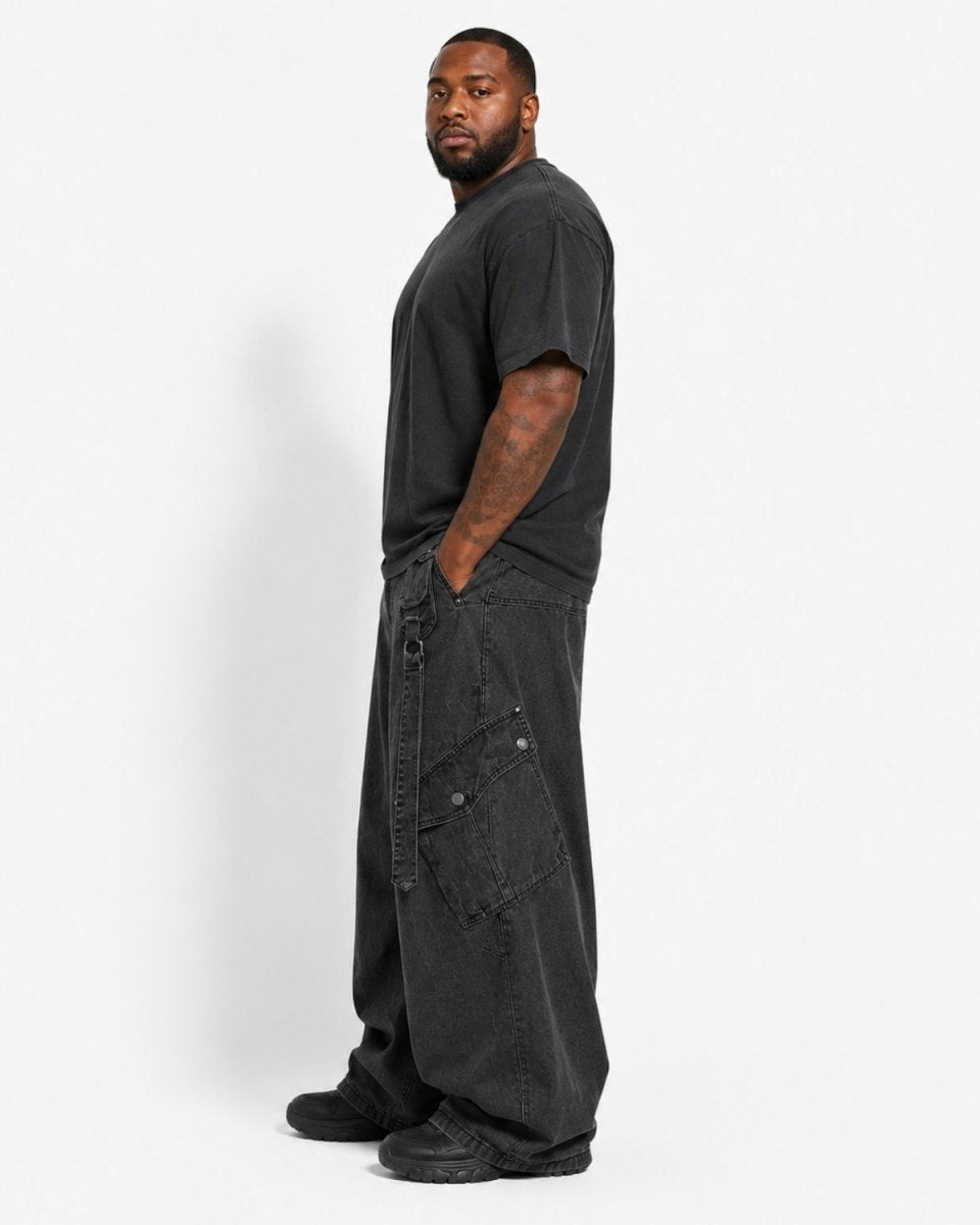 A man wearing a black crewneck t-shirt and oversized black cargo pants, standing in profile against a light gray studio background.