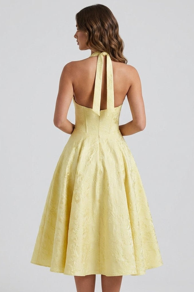 Back view of a model wearing the Kouvr yellow open back halter midi dress showcasing the fitted corset waist and textured fabric.