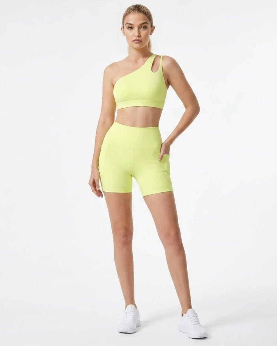 Woman wearing yellow asymmetric one shoulder sports bra and high waisted biker shorts set with pockets front full body view