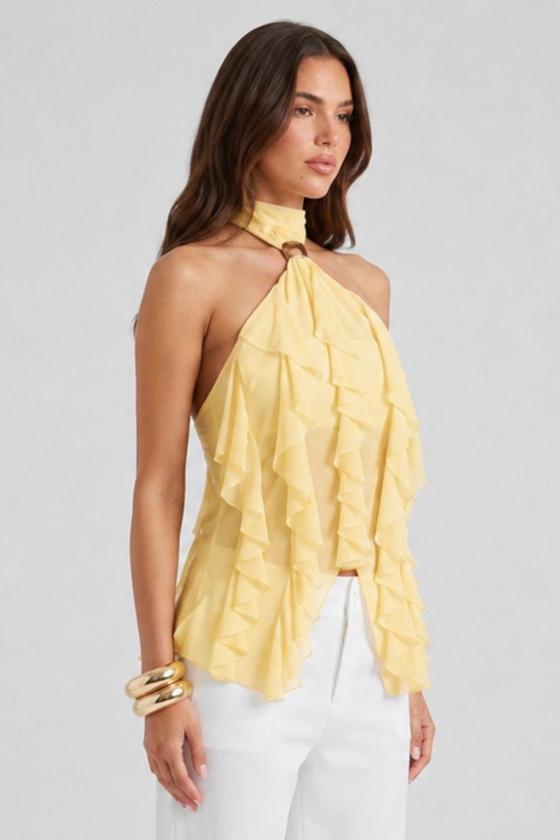 A woman wearing a pale yellow ruffled halter-neck top and white pants, posed against a light gray studio background.